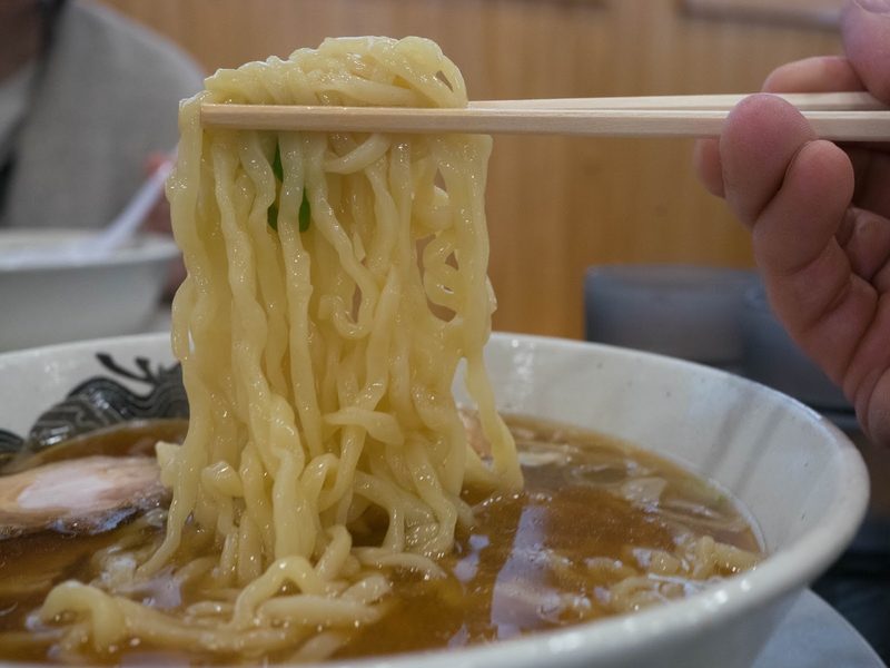 箸で持ち上げた喜多方ラーメンの平打ち縮れ麺